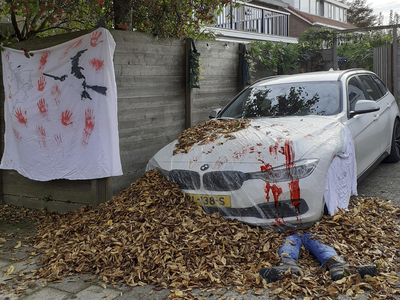 902725 Afbeelding van een 'lijk' onder een auto, als versiering ter gelegenheid van Halloween, achter de woning ...
